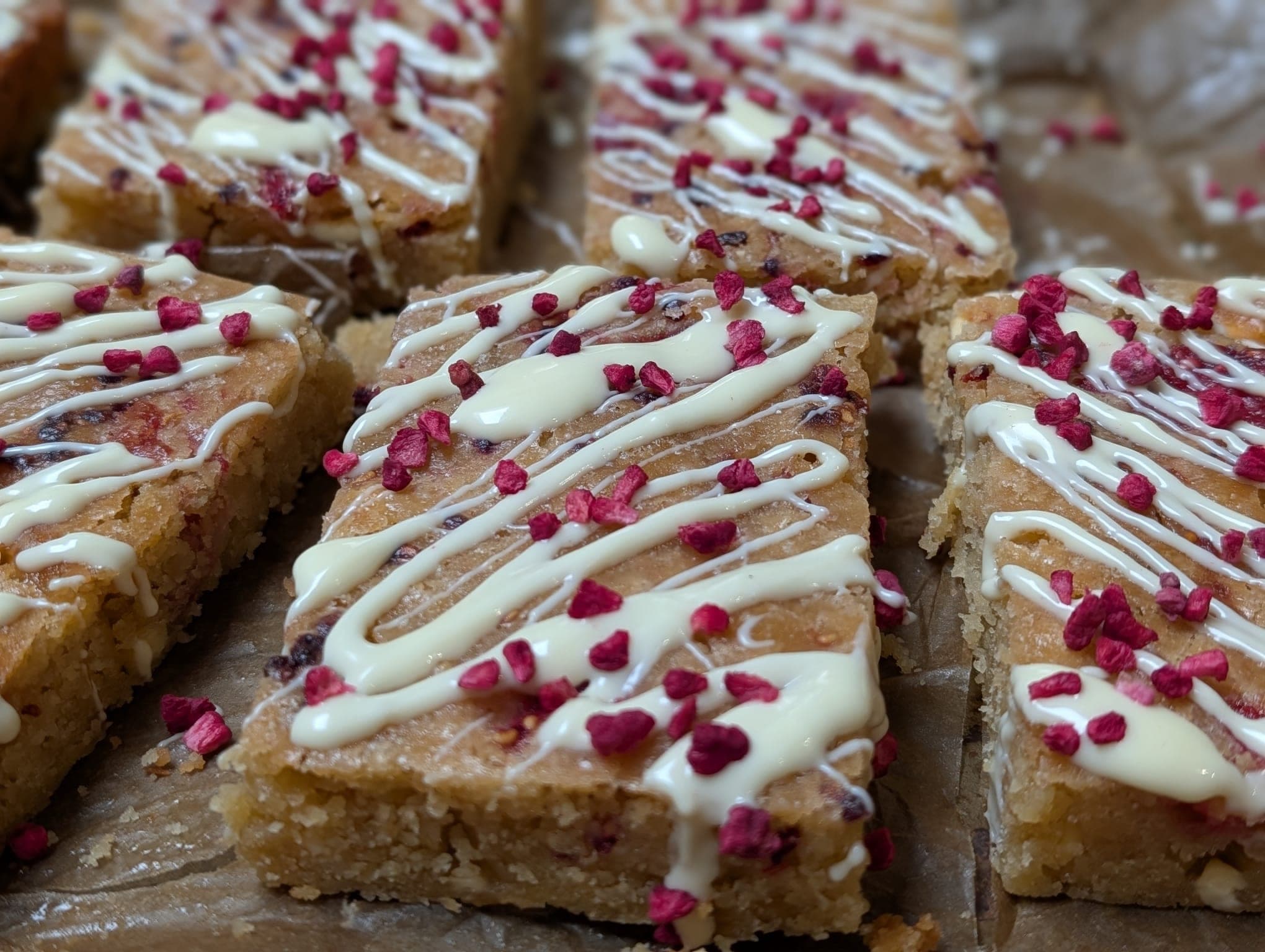 Slices of white chocolate blondie drizzled with white chocolate and topped with freeze-dried raspberries